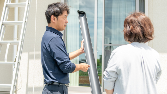 雨どいのパーツを持って、お客様に説明している様子
